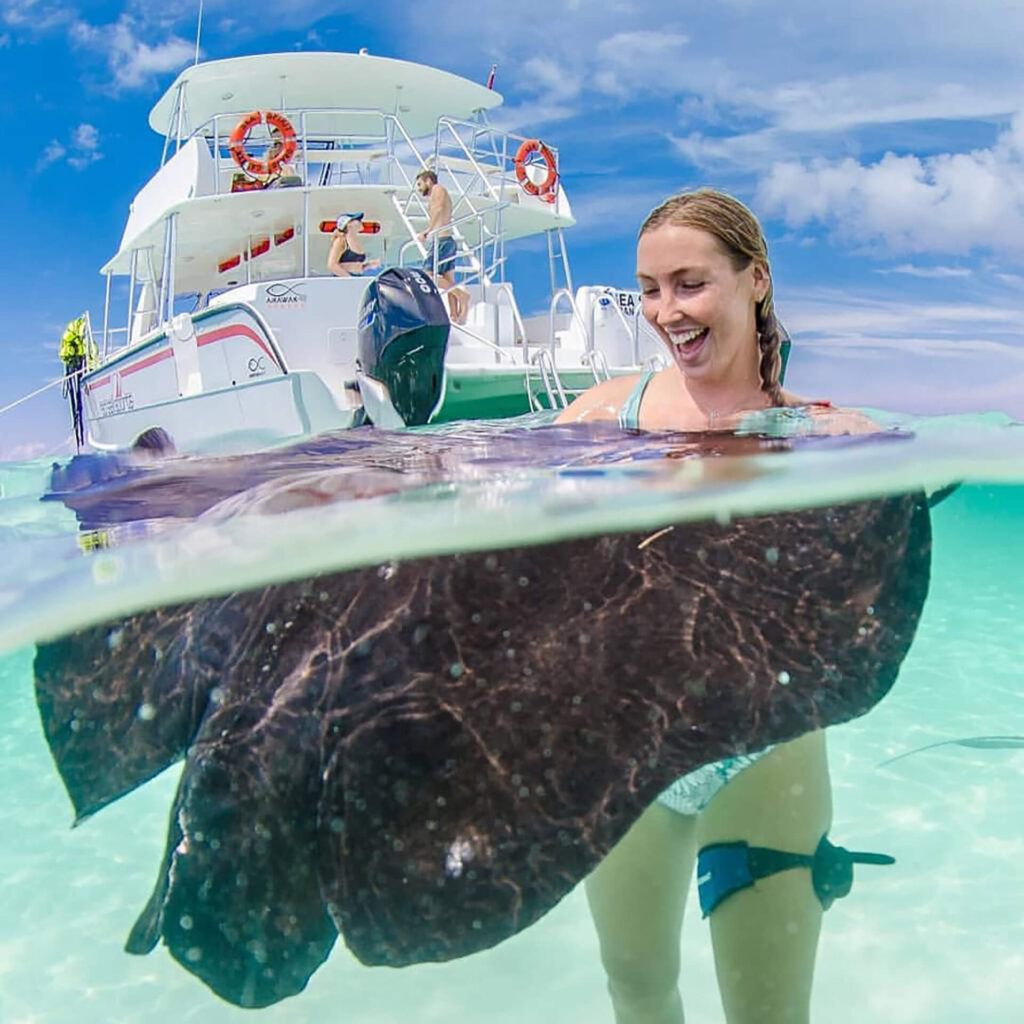 A woman is holding a sting ray at Rum Point Beach Club in Grand Cayman.