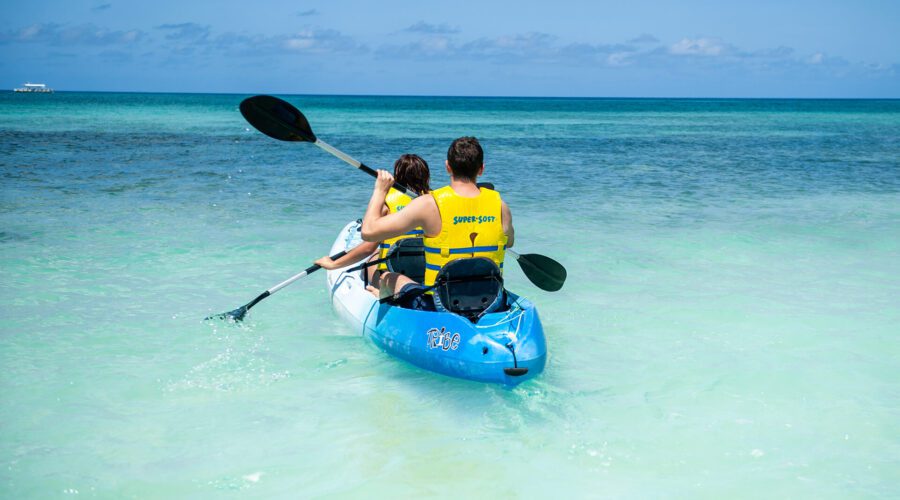 Two people enjoying cocktails while paddling a kayak in the ocean at Rum Point Beach Club.