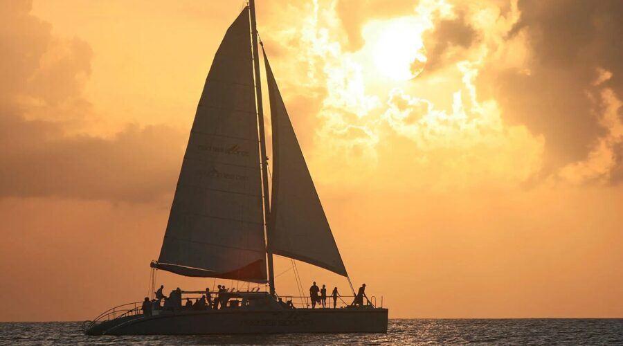 A catamaran sails in the ocean during a stunning sunset