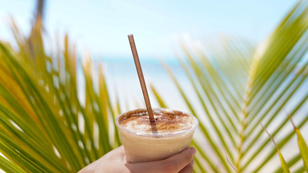 A person holding a mudslide drink in front of palm trees.