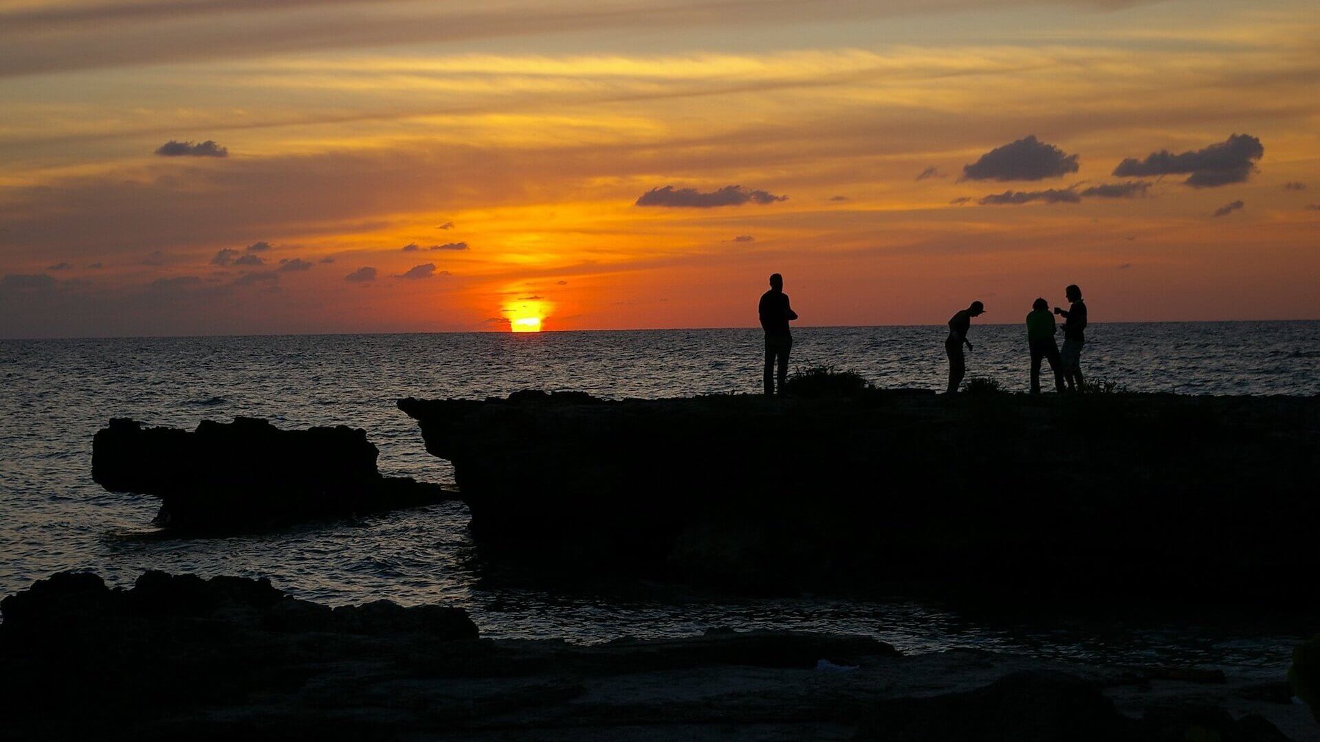 A group of people standing on a rocky beach at sunset.